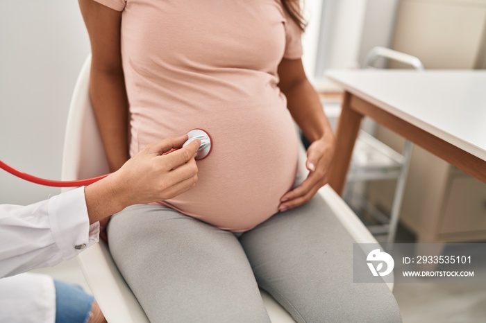 Young latin woman pregnant and doctor auscultating belly at clinic