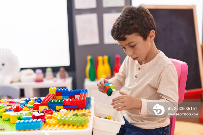 Adorable hispanic boy playing with construction blocks sitting on table at kindergarten