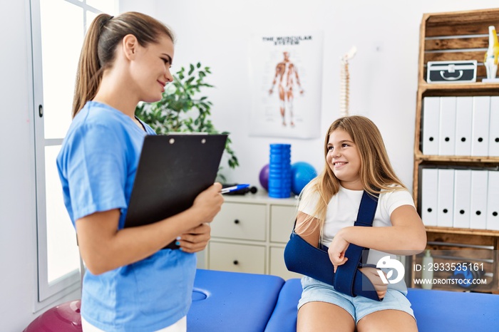 Woman and girl physiotherapist and patient with sling on arm having rehab session at physiotherapy clinic