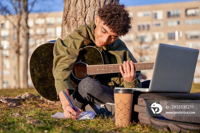 self-taught young man playing and learning to play the guitar with the laptop. teenager composing a song.