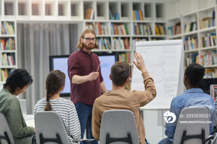 Young businessman standing near the whiteboard and holding the presentation for young people at library