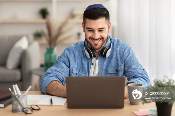 Smiling israeli man working on laptop at home