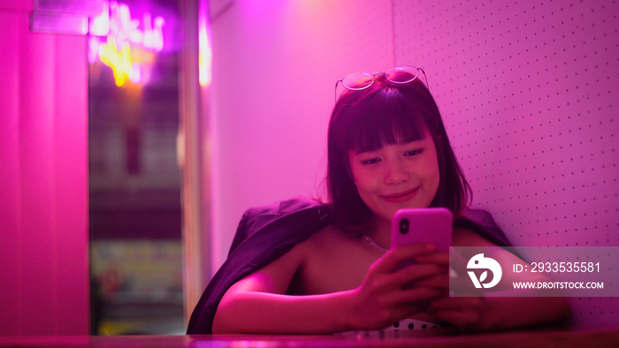 Young beautiful asian millennial teen woman using smartphone in neon night club, lifestyle background