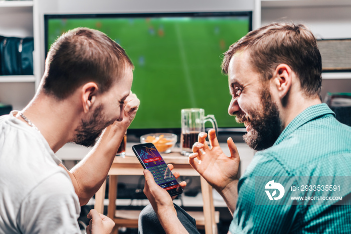 Two male friends watching live football game broadcast on tv