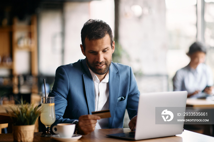 Male entrepreneur using laptop and credit card in cafe.