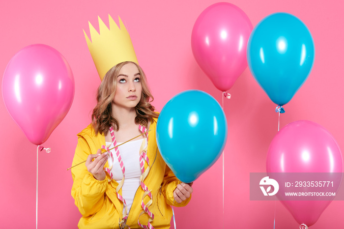 Funny conceptual photography. Cheeky girl in birthday hat holding needle pretending to pop birthday balloons. Attractive trendy teenager celebrating birthday.