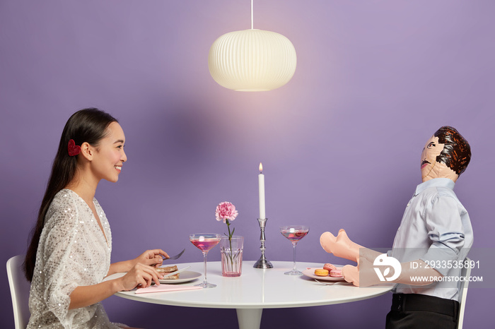 Smiling woman has pleasant talk with mannikin, imitates dating, forgets about real problems with unreal boyfriend, has unrequited love enjoys romantic dinner in cozy restaurant isolated on purple wall