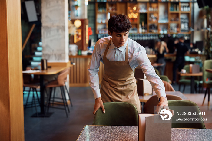 Young waiter setting table while working in cafe.