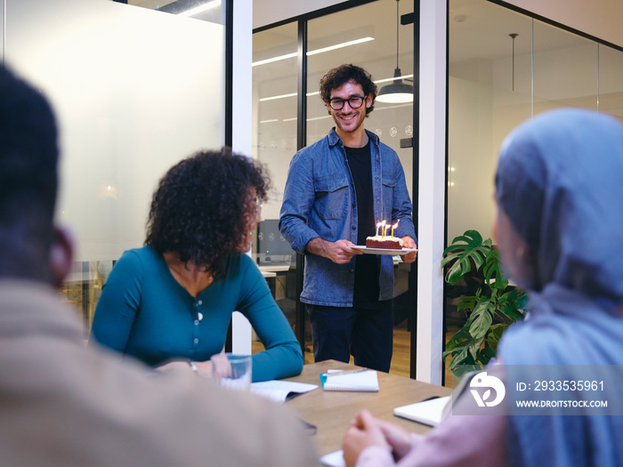 UK, London, Smiling man with birthday cake entering conference room