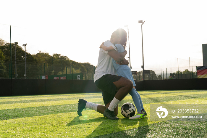 Coach and girl (6-7) hugging on soccer field