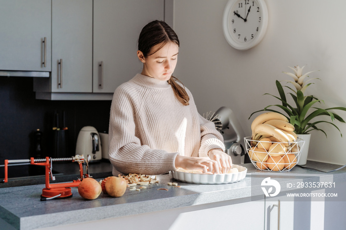 Teen girl putting fresh apple into pie dish making apple pie. Child cooking charlotte at kitchen at home.