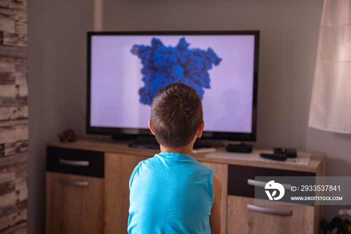 A Little boy watching TV at home. View from behind sofa