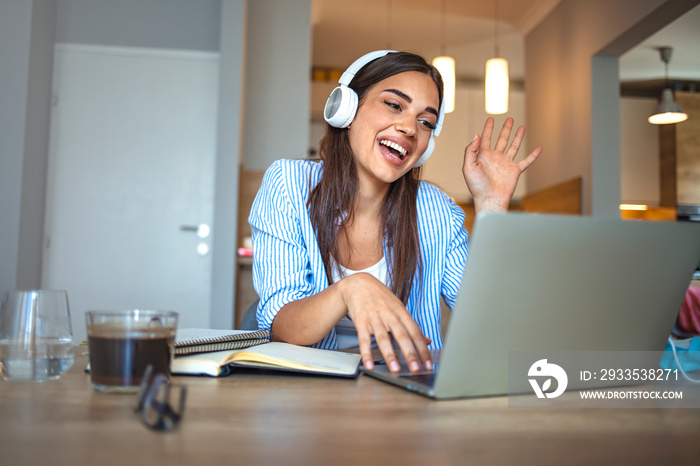 Smiling girl student wear wireless headphone study online with skype teacher, happy young woman learn language listen lecture watch webinar write notes look at laptop sit in cafe, distant education