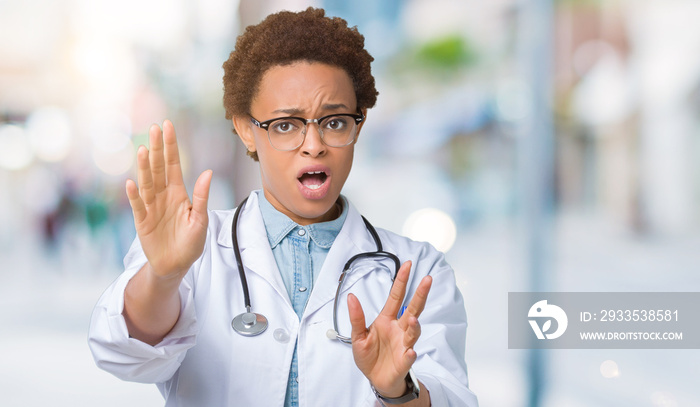 Young african american doctor woman wearing medical coat over isolated background afraid and terrified with fear expression stop gesture with hands, shouting in shock. Panic concept.