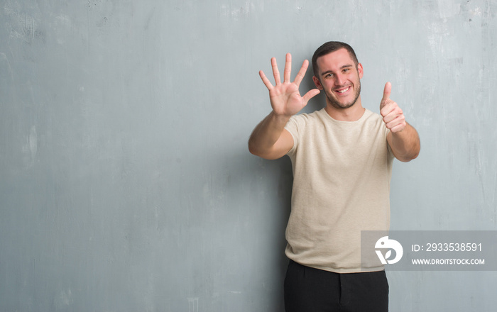 Young caucasian man over grey grunge wall showing and pointing up with fingers number six while smiling confident and happy.