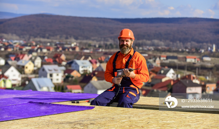 builder use drill. Build your future yourself. Flat roof installation. roofing felt. Roofer worker in special protective work wear. new roof under construction residential building