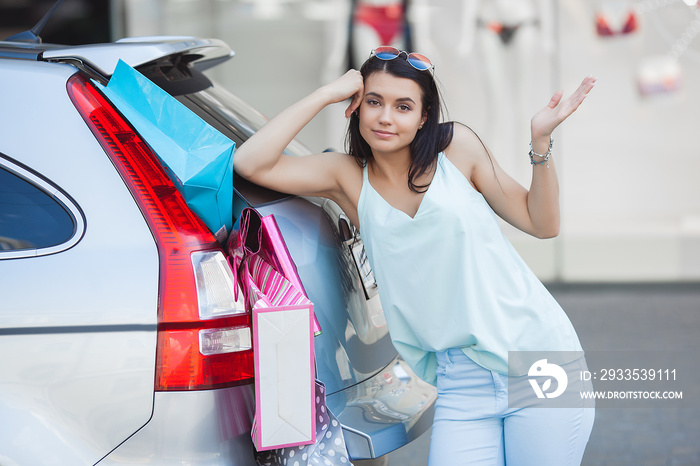 Attractive young girl trying to put a lot of retails into a car. Woman putting shopping bags into a luggage. Young female shoving up her shopping bags into a trunk.