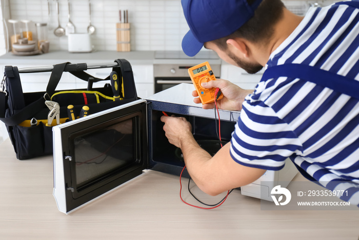 Young man repairing microwave oven in kitchen