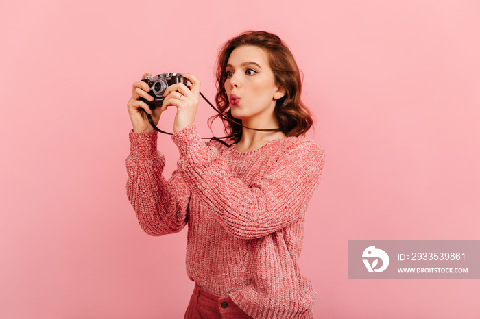 Surprised girl taking photos. Studio shot of pretty woman with camera isolated on pink background.