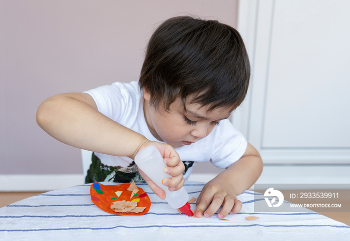 Preschool kid putting glue stick on paper for his school homework, Cute little boy using colour paper making easter eggs for DIY project, Portrait child learn to to using glue sticking together