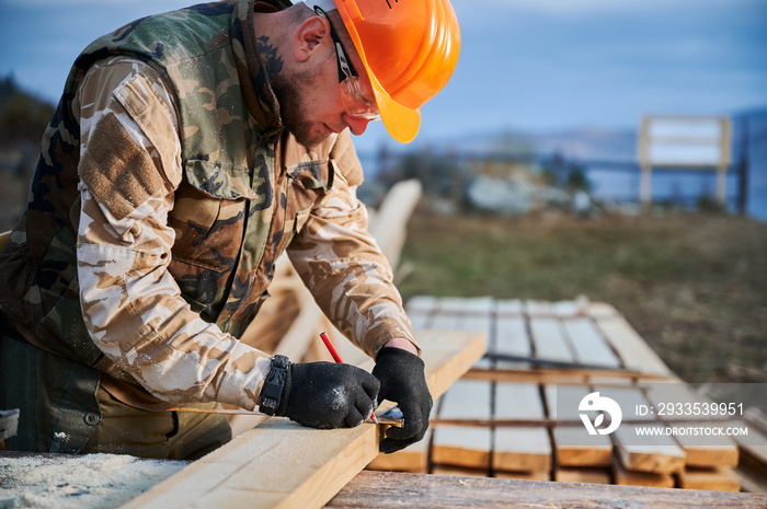 Man worker building wooden frame house. Carpenter measuring wooden planks and making marks with pencil. Carpentry concept.