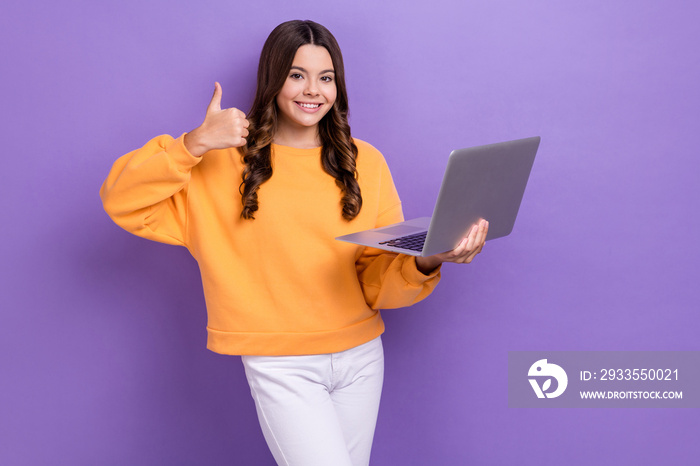 Photo of adorable cool girl dressed orange sweatshirt showing thumb up typing device empty space isolated purple color background