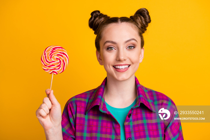 Close-up portrait of her she nice attractive pretty lovely cheerful cheery girl wearing checked shirt holding in hand striped lollypop isolated bright vivid shine vibrant yellow color background