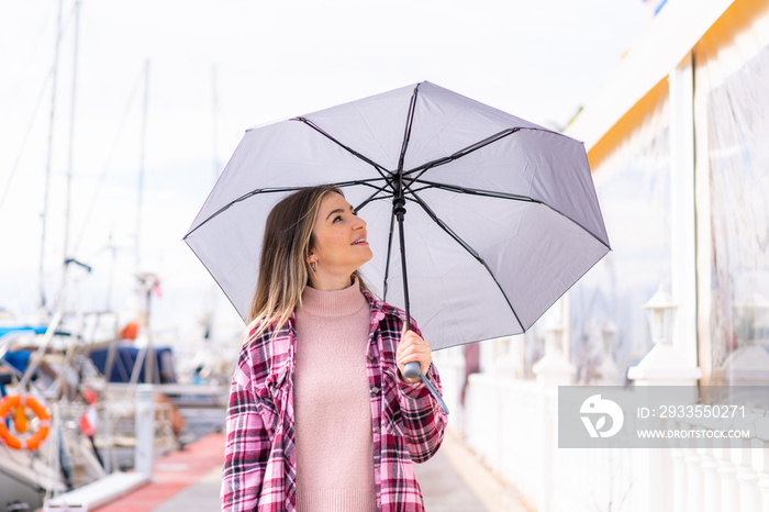 Young pretty Romanian woman holding an umbrella at outdoors with happy expression