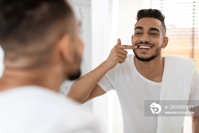 Dental Health. Handsome Arab Man Looking In Mirror At His White Teeth