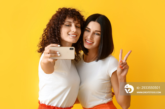 Young sisters showing victory gesture and taking selfie on color background