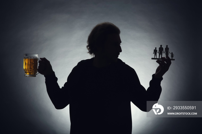 Silhouette of man with mug of beer and figure on dark background. Concept of choice between alcohol and family