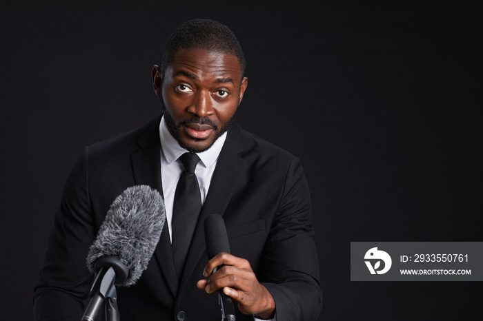 Portrait of confident African-American man standing at podium and giving speech against black background, copy space