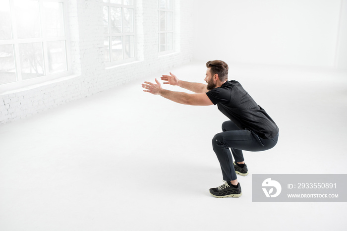 Handsome man in the black sportswear holding plank in the white gym interior