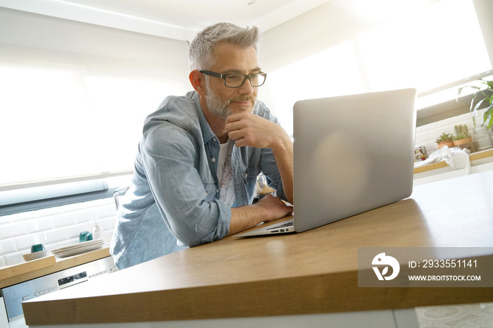 Man looking on computer at home in modern kitchen