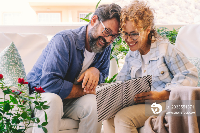 Happy and cheerful man and woman reading together a notebook outside at home. Enjoyed caucasian couple takes notes and read with smile. Adults people at home