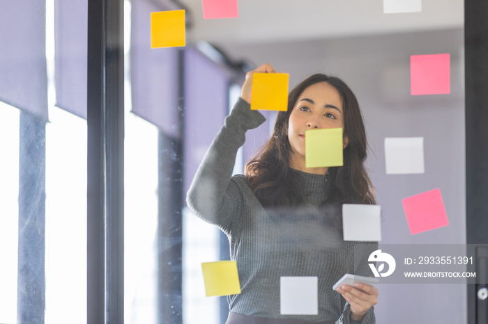 Business female employee with many conflicting priorities arranging sticky notes commenting and brainstorming on work priorities colleague in a modern office.