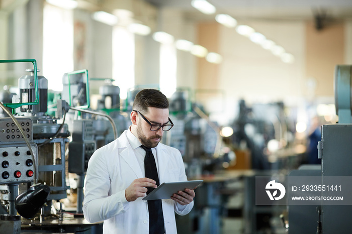 Waist up portrait of handsome factory worker wearing lab coat using digital tablet in industrial workshop, copy space