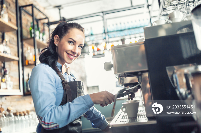 Beautiful barista makes espresso on a professional coffee maker in a cafe