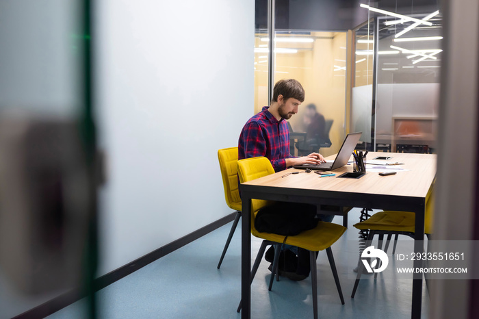 Young businessman working at his desk in the office on a laptop. Business, co-working, online training. Side view