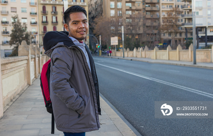 waist up image of a mexican exchange student standing on a bridge with hands in pockets looking at the camera