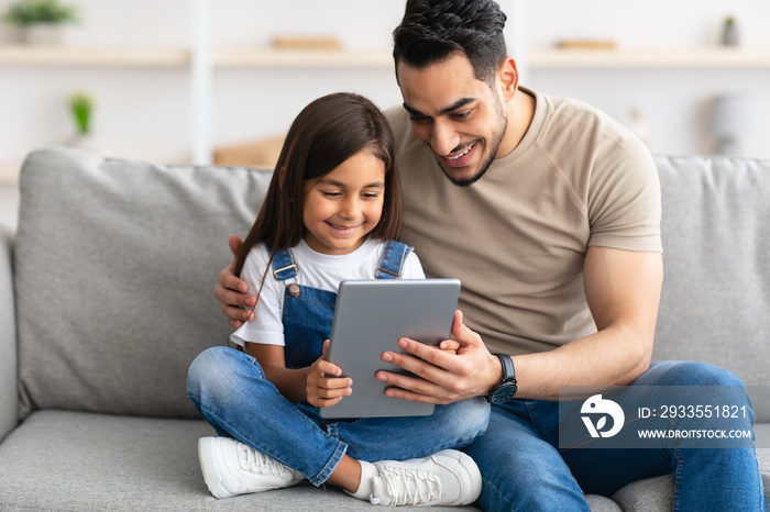 Smiling dad and daughter sitting on couch, using tablet