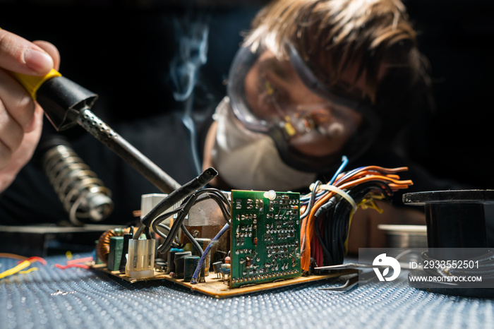 A man in glasses and a mask, with a soldering iron, repairs equipment