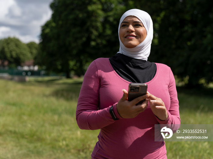 UK,Sutton,Woman in headscarf holding smart phone in park