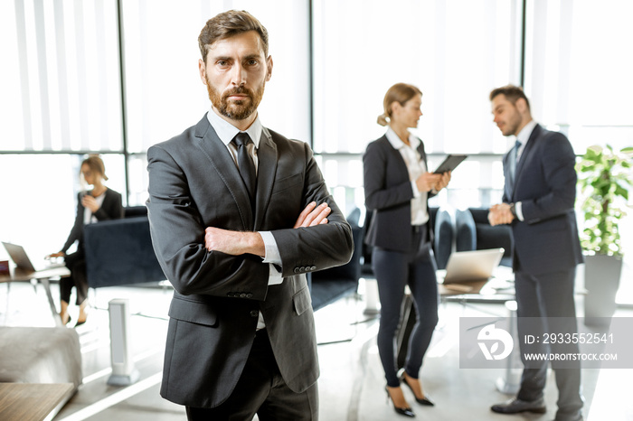 Portrait of a handsome white collar worker standing in front of business team at the luxurious office