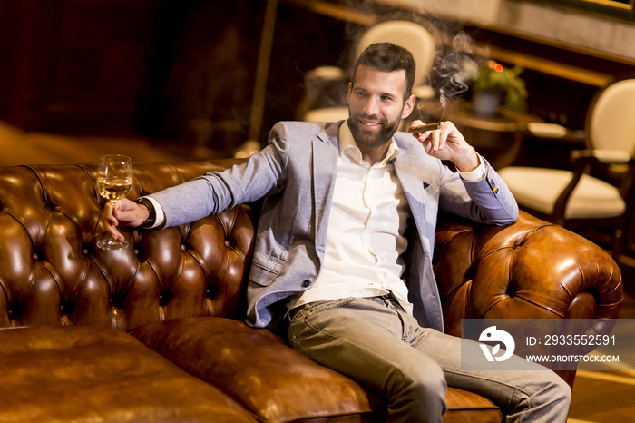 Young man tasting white wine and smoking cigar