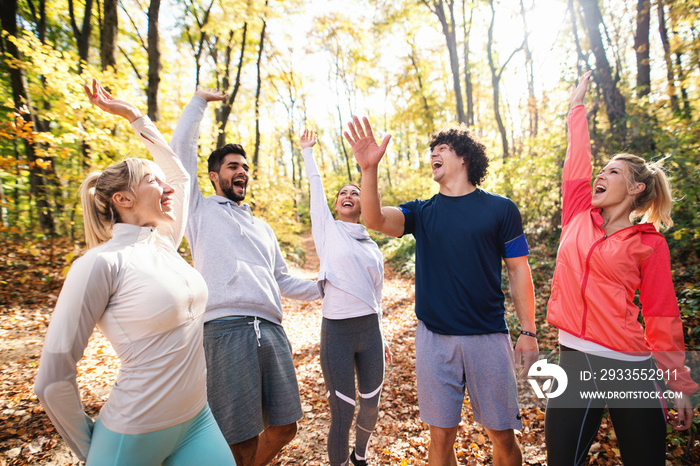 Happy group of runners smiling and stacking hands while standing in woods in autumn.