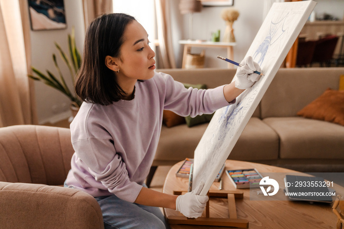 Beautiful asian girl artist drawing with pencil on canvas while sitting at home