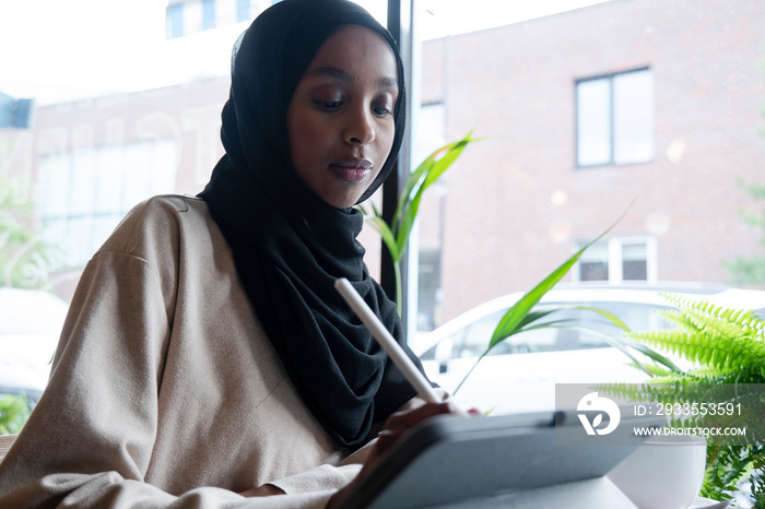 Young woman in hijab working on tablet in cafe
