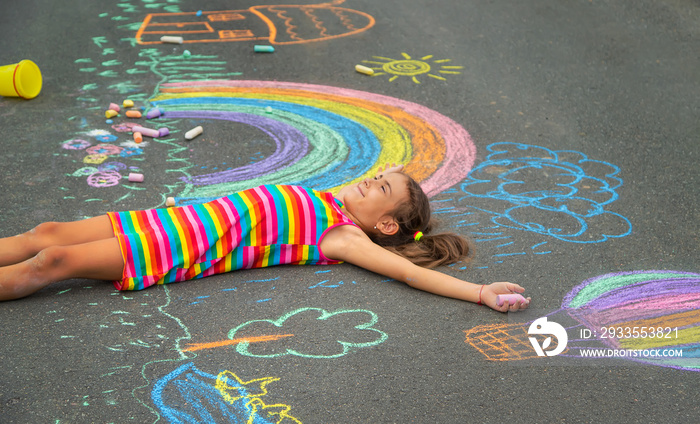 The child draws with chalk on the asphalt. Selective focus.