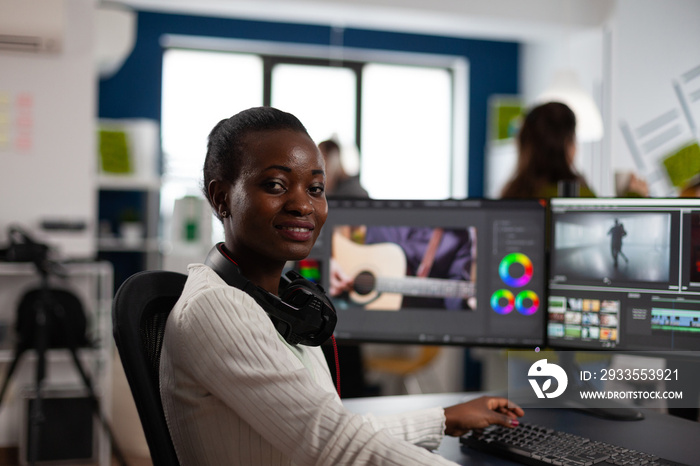 African american video editor artist looking at camera smiling editing creative video project in post production software working in startup studio office. Videographer editing audio film montage